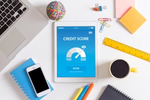 Does matched betting affect your credit score? A flat lay shot of a desktop showing a tablet with a credit score diagram on the screen, surrounded by an iphone, a laptop, a coffee cup, pens, notebooks and other small items of stationery.