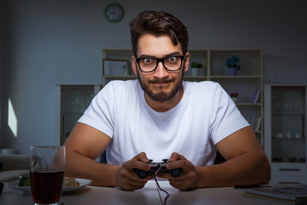 A man, engrossed in a video game, sits at a table with a video game controller.