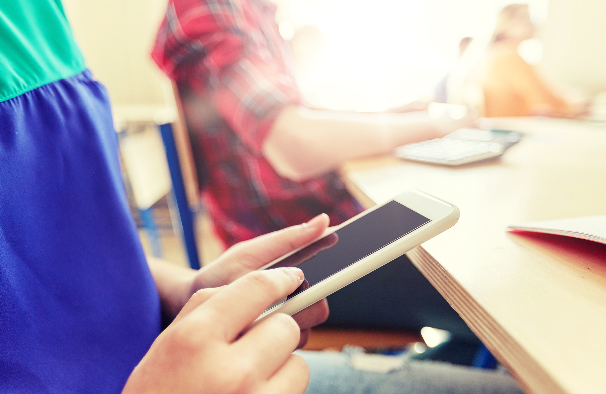 A student multitasking on their mobile phone in a classroom, potentially searching for online jobs opportunities.