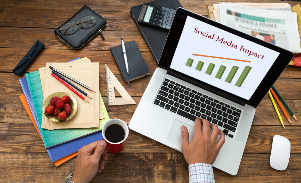 A flat lay image of a social media manager's desk, showing a lap top, coffee, bowl of berries and several notebooks and stationery items. Social media manager is one way to make extra cash in the UK