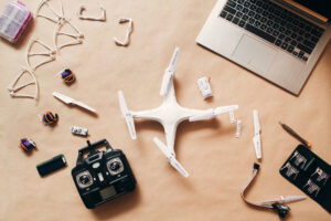 Drone with remote control and laptop, flat lay. Top view on table with laptop, white quadrocopter with transmitter and elements for it.