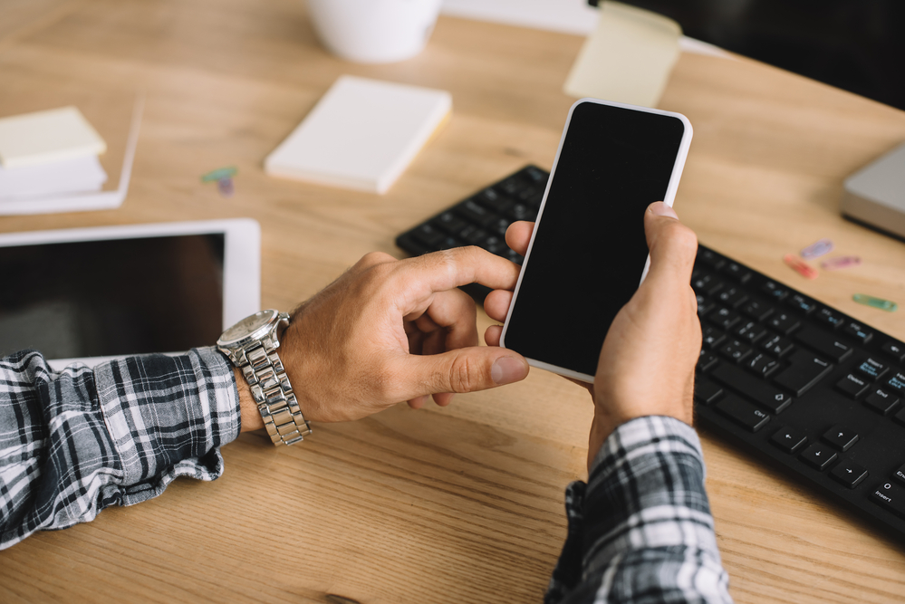 A person is using a smartphone at a desk to contact a gambling support hotline.