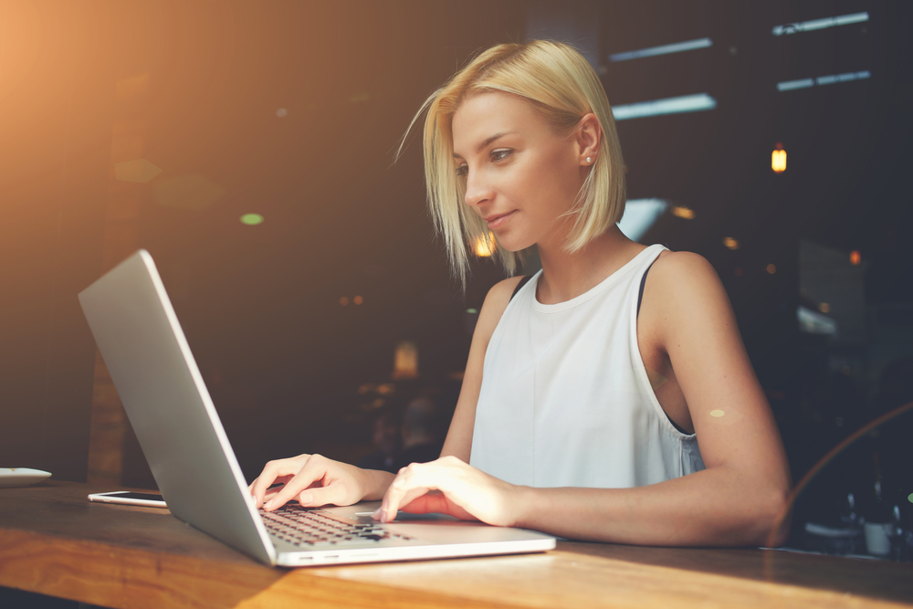 Young, nicely dressed woman working on laptop which is on a wooden desk