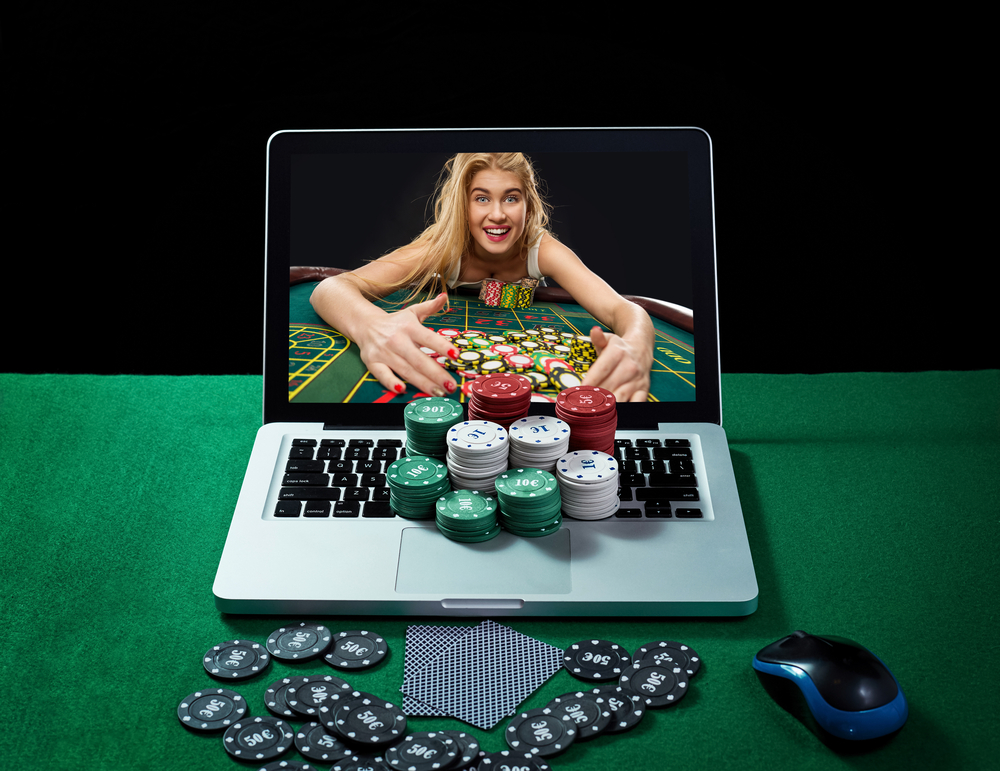 Green table with casino chips, cards on notebook, image of poker player on screen of laptop. 