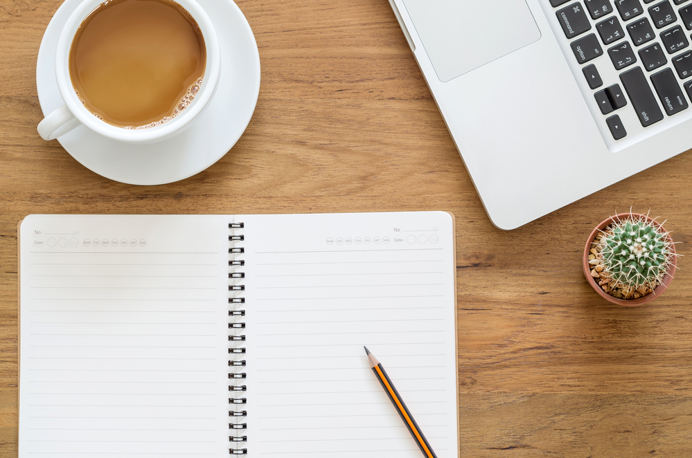 Flat lay of a coffee cup,  notebook and a laptop with matched betting tips on a rustic wooden table.