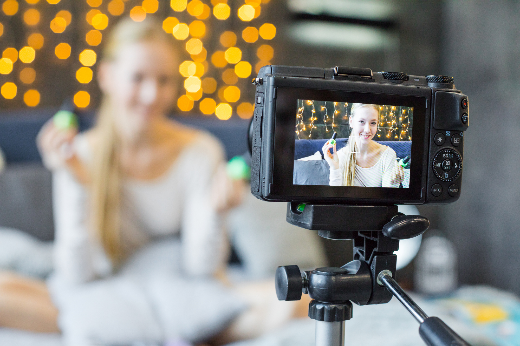 A female student influencer is sitting on a bed, recording a video with a camera for her online job.