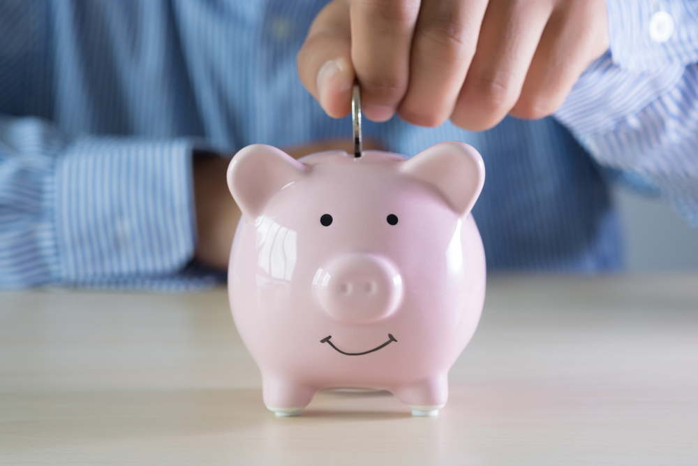 a hand putting a coin into a smiley-faced piggy bank 