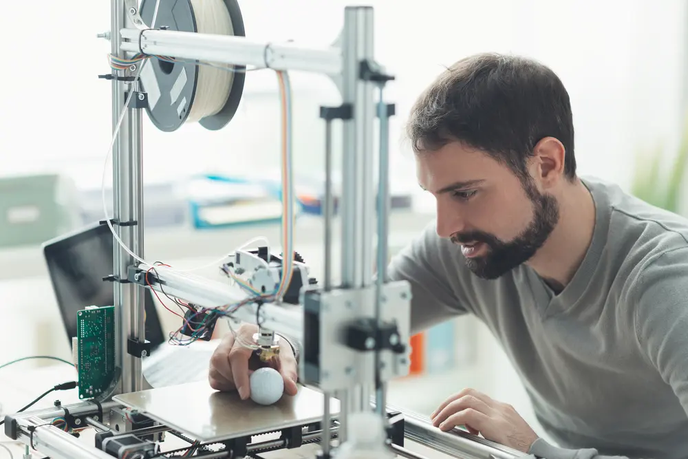 A man using a 3D printer at home. There's a start up cost, but you don't need special skills and you can use your 3D printer to make money.