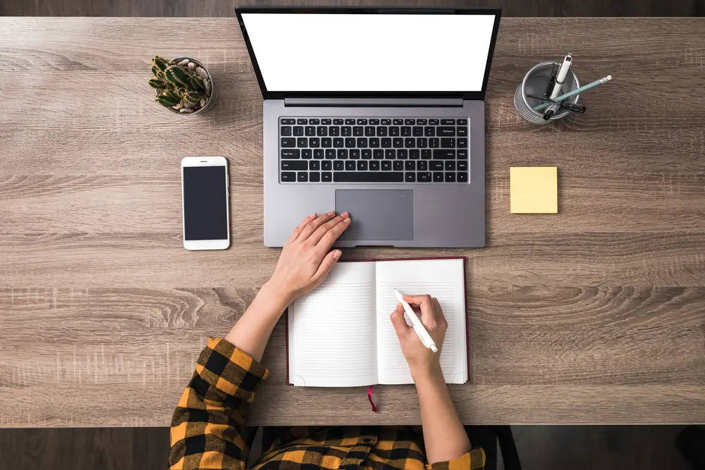 a flat lay showing the desk of a freelance writer working online with a notepad and laptop