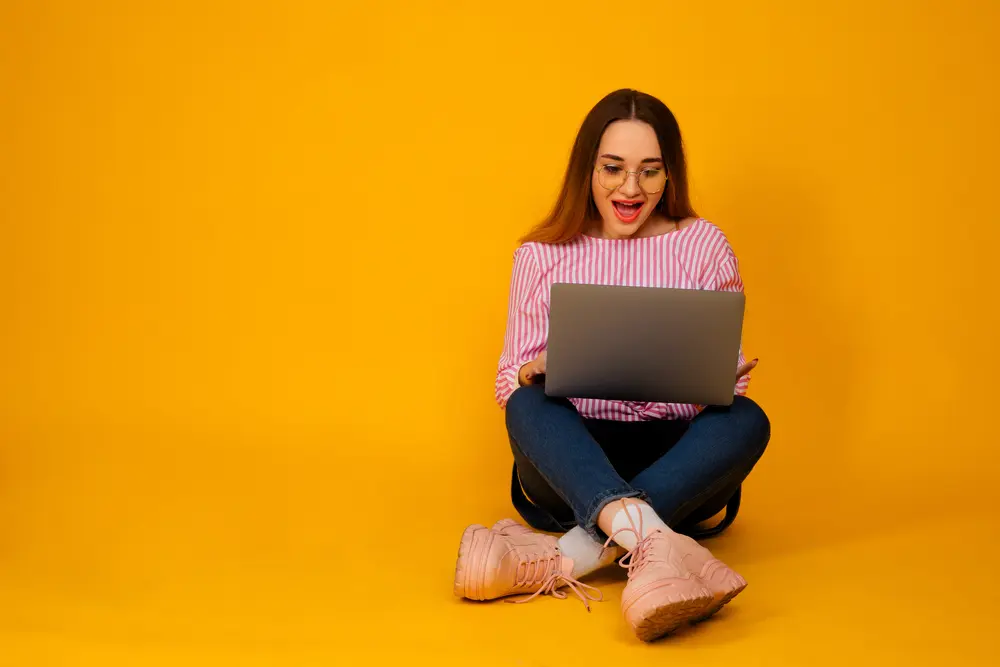 woman in red shirt and jeans chatting online on her laptop on yellow background