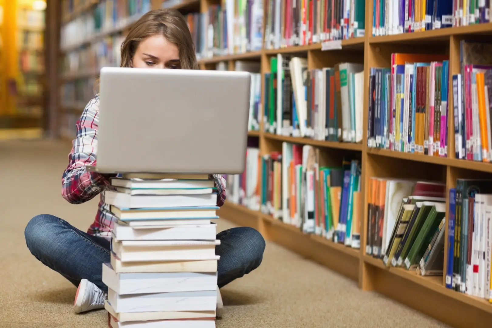 a student working with a laptop and a pile of books in a library