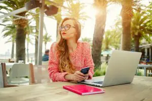 a female blogger sitting at her laptop with mobile phone at an outside desk in exotic location