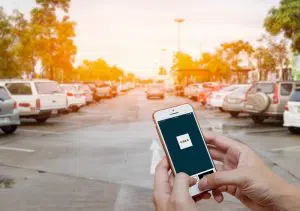 a man's hands holding an iphone with the Uber app on the screen. The background is a carpark.