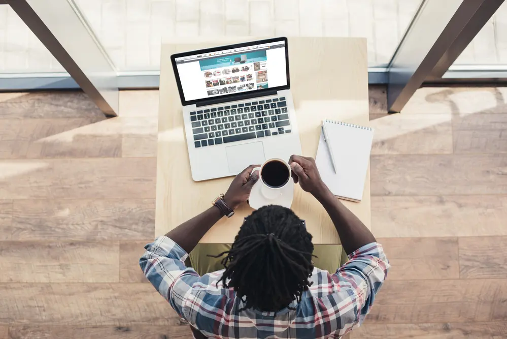 a man sitting at his laptop drinking coffee doing AMazon FBA product research on the Amazon website