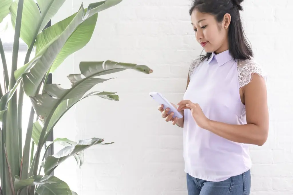 fashionable girl looking at her phone against a white brick wall